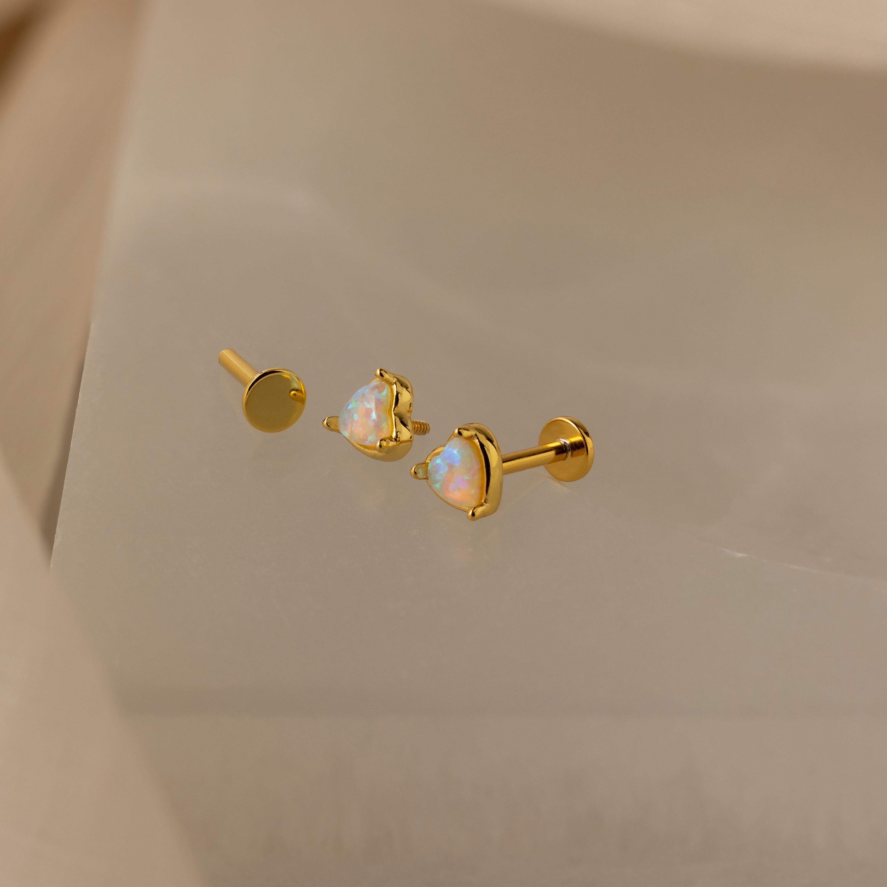 A pair of heart-shaped flat-back stud earrings with opal gemstones, displayed on a white surface.